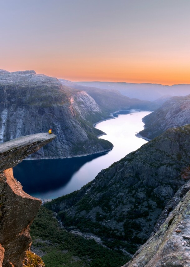 Fjordlandschaft mit Person auf einer Felsklippe bei Sonnenuntergang.