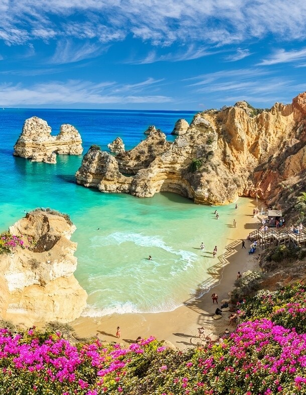 Blick von oben auf eine von Felsen umgebende Bucht und türkisblaues Meer an der Algarve.