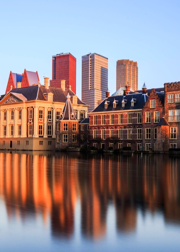 Skyline von Den Haag bei Sonnenuntergang, die Gebäude spiegeln sich im Wasser.