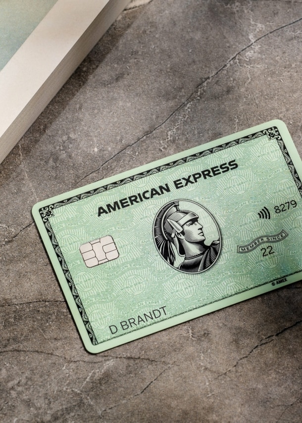 ine grüne American Express Kreditkarte liegt auf einem grauen Marmortisch neben einem Buch.