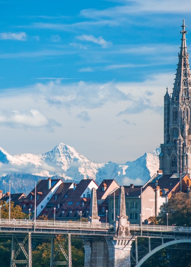 Turm der Kathedrale von Bern mit schneebedeckten Gipfeln im Hintergrund.