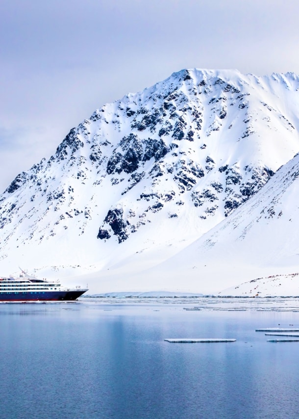 Ein Expeditionsschiff im arktischen Gewässer vor schneebedeckten Bergen.