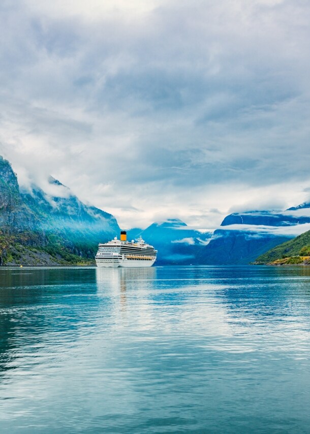 Kreuzfahrtschiff in wolkenverhangener Fjordlandschaft.