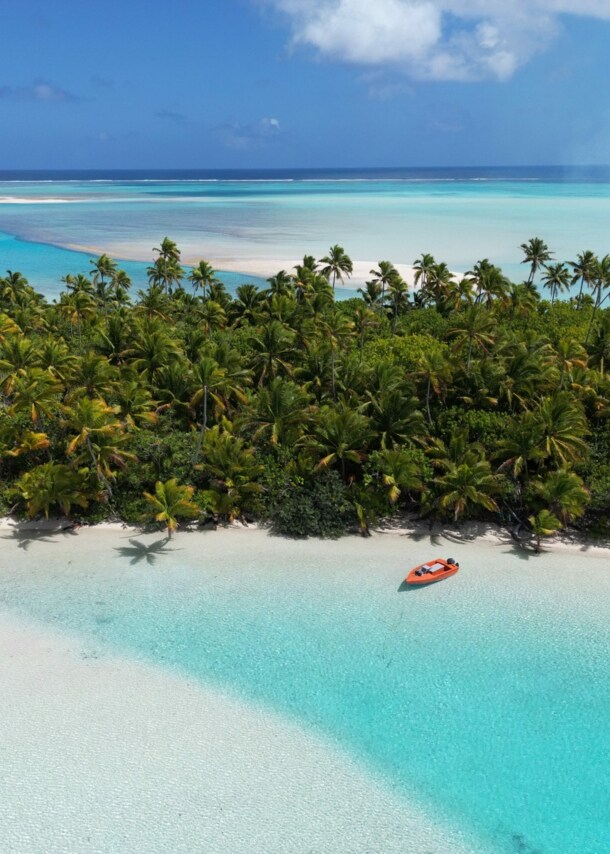 Südseeinsel mit Palmenwald an einer trürkisblauen Lagune mit weißem Sandstrand.