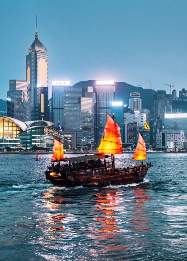 Rote chinesische Dschunke auf dem Wasser vor der Skyline Hongkongs bei Nacht.