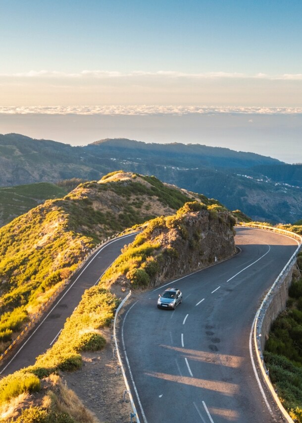 Ein Auto auf einer kurvigen Straße durch eine hügelige Landschaft auf Madeira.