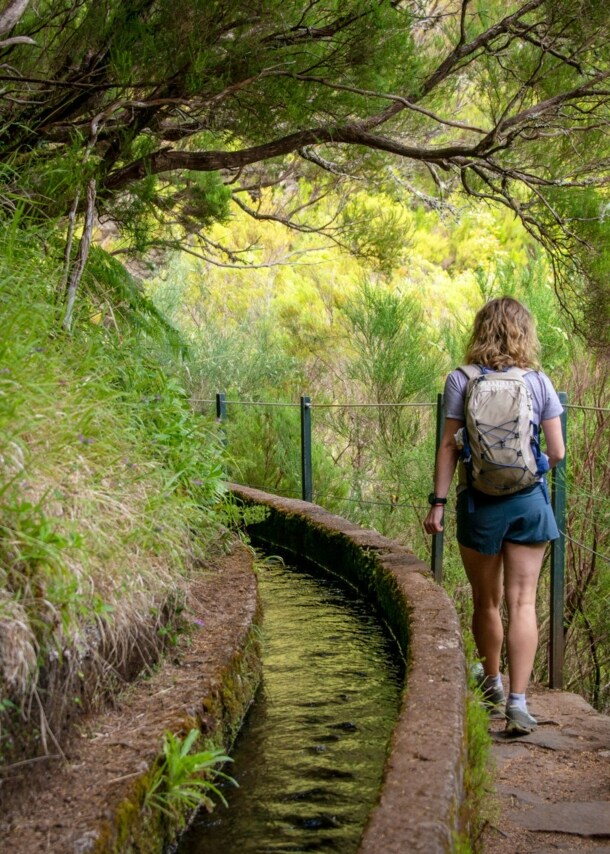 Rückansicht einer Frau auf einem Wanderweg auf Madeira, der entlang eines Bewässerungskanals verläuft.