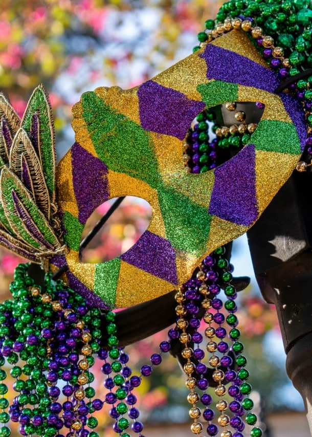 Eine Maske und Perlenketten in den Farben Grün, Gold und Violett an einer Straßenlaterne.