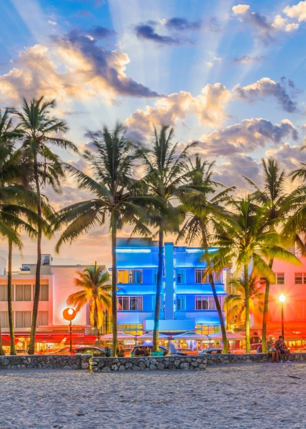 Strandpromenade mit Palmen und Art-déco-Gebäuden mit Neon-Beleuchtung am Abend.