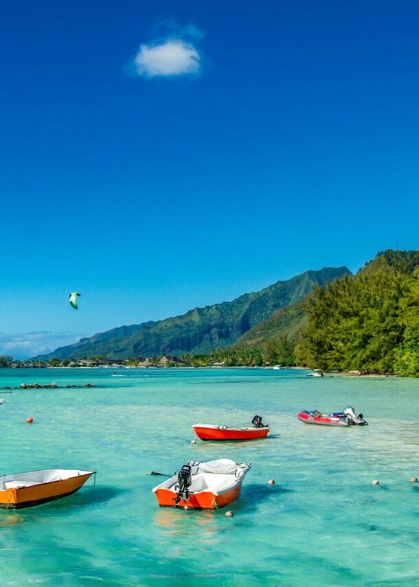 Kleine Boote im türkisblauen Wasser an einem Sandstrand mit tropischer Vegetation.