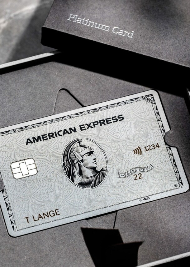 American Express Platinum Card aus Metall in einer geöffneten Präsentationsbox aus grauer Feinkartonage auf einem Marmortisch.