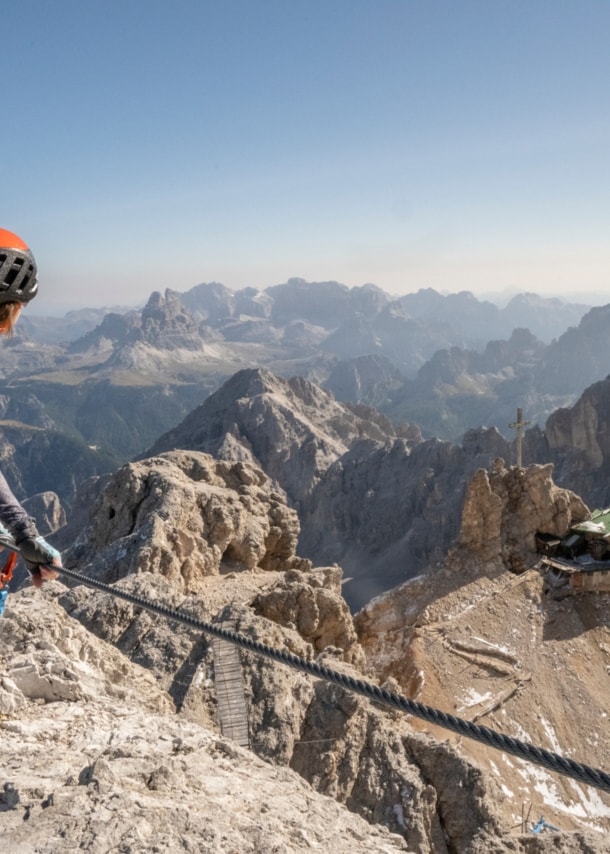 Eine Person mit Kletterausrüstung, die sich an einem Seil festhält, im Hintergrund Berge.