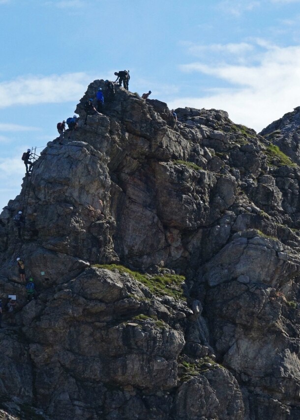 Mehrere Personen, die einen Felsen am Hindelanger Klettersteig erklimmen.