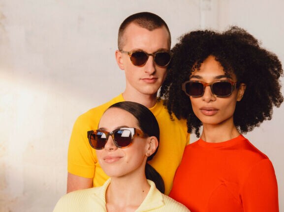Drei Personen mit einfarbigen Oberteilen und Sonnenbrillen