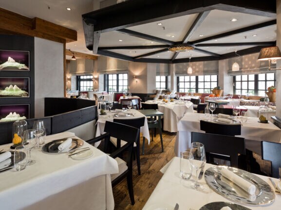 Elegantes Restaurant mit schwarzen Holzstühlen an eingedeckten Tischen mit weißen Tischdecken.