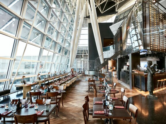 Eingedeckte Esstische eines stilvollen Restaurants mit Panoramafenstern in einem Flughafenterminal.