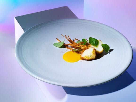 Stillleben einer reduzierten, kunstvoll angerichteten Speise auf einem großen weißen Teller auf einem weißen Block.