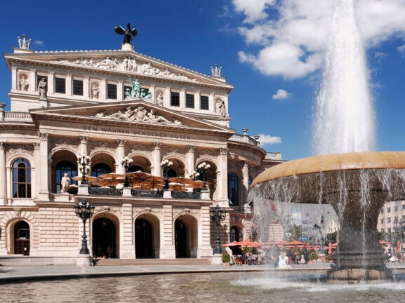 Prachtvolles Operngebäude im Stil der Neorenaissance mit Restaurant, im Vordergrund ein Springbrunnen.