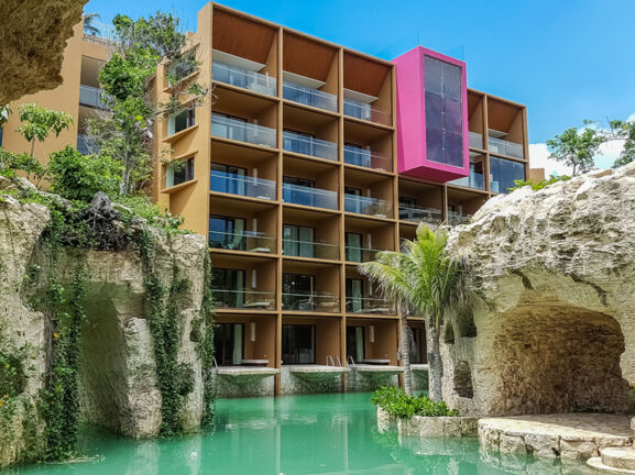 Moderner Hotelkomplex, umgeben von bepflanzten Felsen an einem Pool mit türkisfarbenem Wasser.