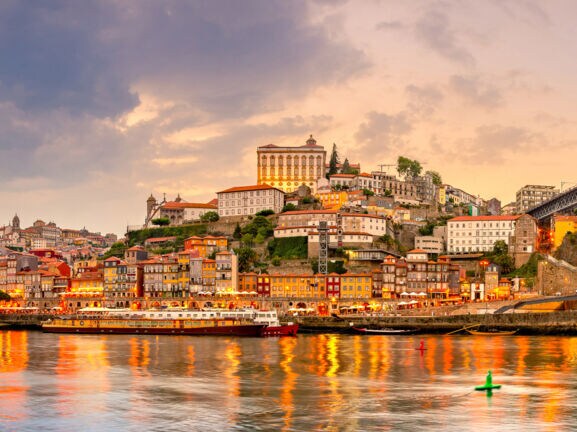 Panoramaaufnahme der Stadt Porto bei Sonnenuntergang mit dem Fluss Duoro im Vordergrund.