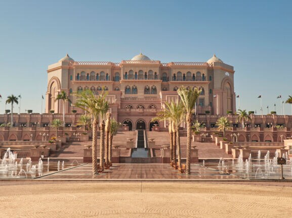 Außenansicht des Emirates Palace Mandarin Oriental Hotels in Abu Dhabi mit Palmen und Brunnen im Vordergrund.