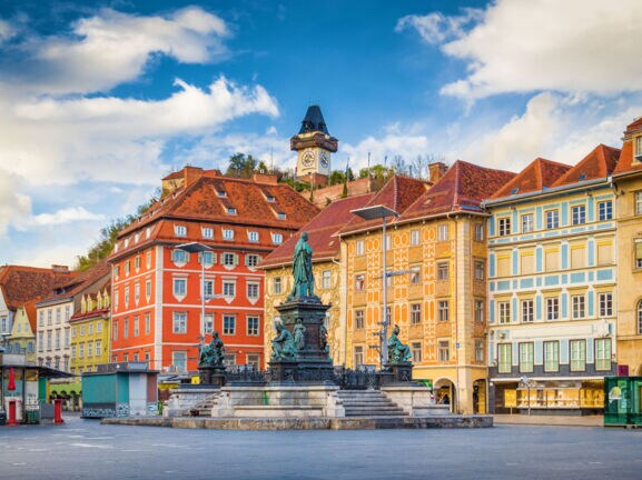 Marktplatz mit Brunnen vor bunter Häuserfassade in der Altstadt von Graz.