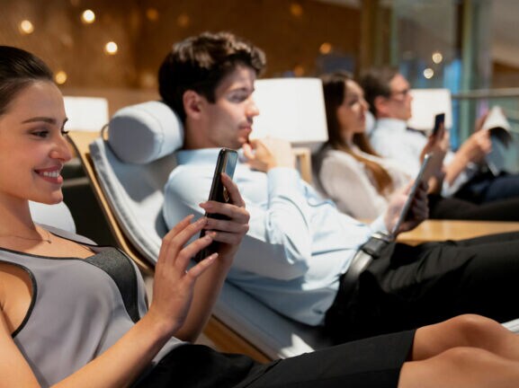 Vier Personen nebeneinander auf Liegen in einer Flughafen-Lounge.