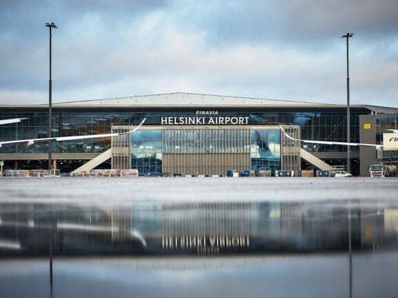 Helsinki Flughafenterminal mit Flugzeugen, im Vordergrund Spiegelung des Gebäudes auf nassem Rollfeld.