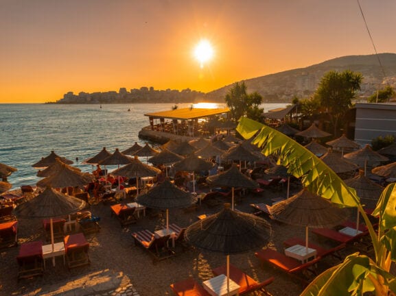 Sandstrand mit Sonnenliegen und Sonnenschirmen aus Stroh bei Sonnenuntergang.