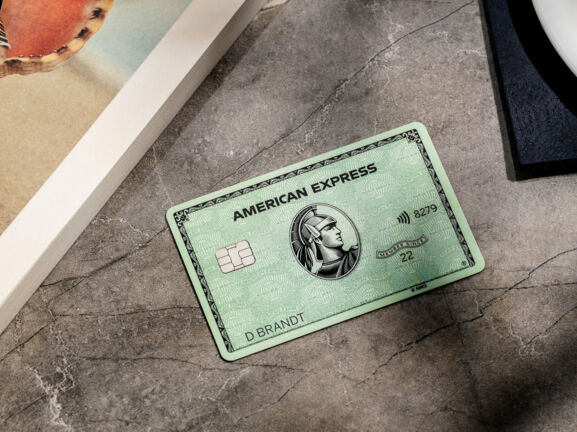 ine grüne American Express Kreditkarte liegt auf einem grauen Marmortisch neben einem Buch.