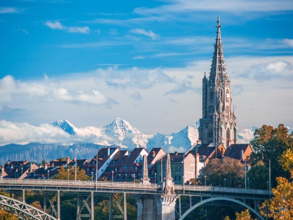 Turm der Kathedrale von Bern mit schneebedeckten Gipfeln im Hintergrund.