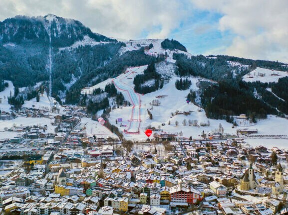 Schneebedecktes Stadtpanorama von Kitzbühel vor Berg mit Skipisten.