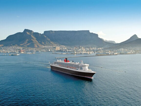 Kreuzfahrtschiff Queen Mary 2 im Wasser vor der Skyline Kapstadts.