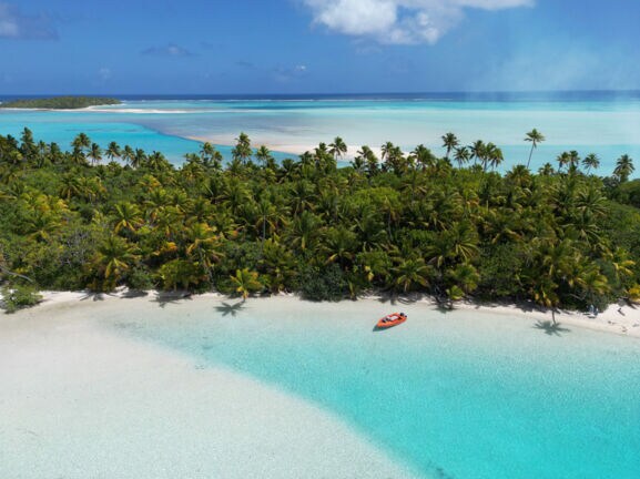 Südseeinsel mit Palmenwald an einer trürkisblauen Lagune mit weißem Sandstrand.