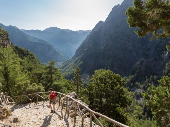 Eine Person beim Wandern in der Samaria-Schlucht auf Kreta, im Hintergrund Vegetation und Berggipfel.