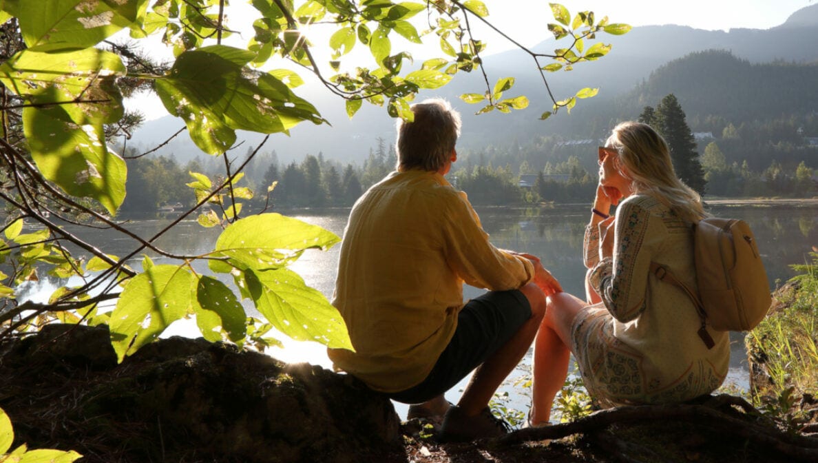 Zwei Personen sitzen in der Natur und schauen auf einen See