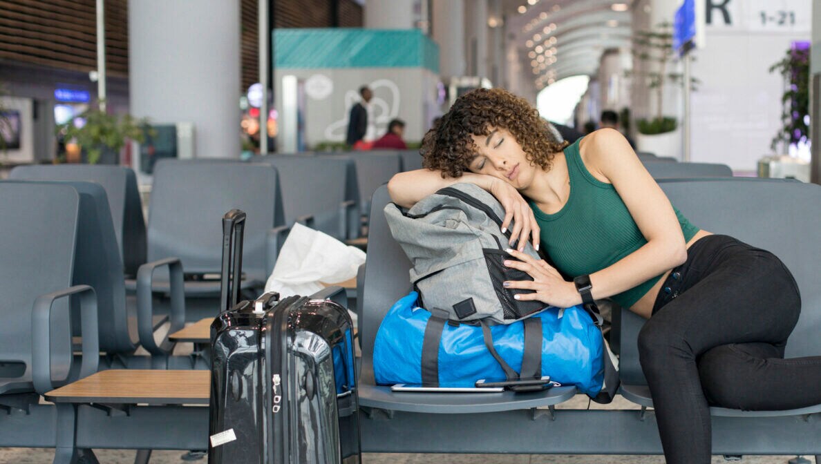 Eine Reisende schläft auf ihr Gepäck gestützt am Flughafen.