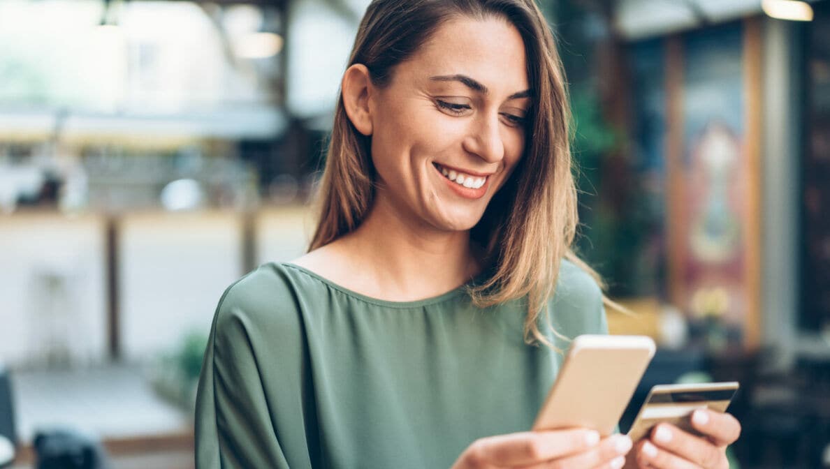 Eine Frau hält lächelnd ein Handy und eine Kreditkarte in den Händen