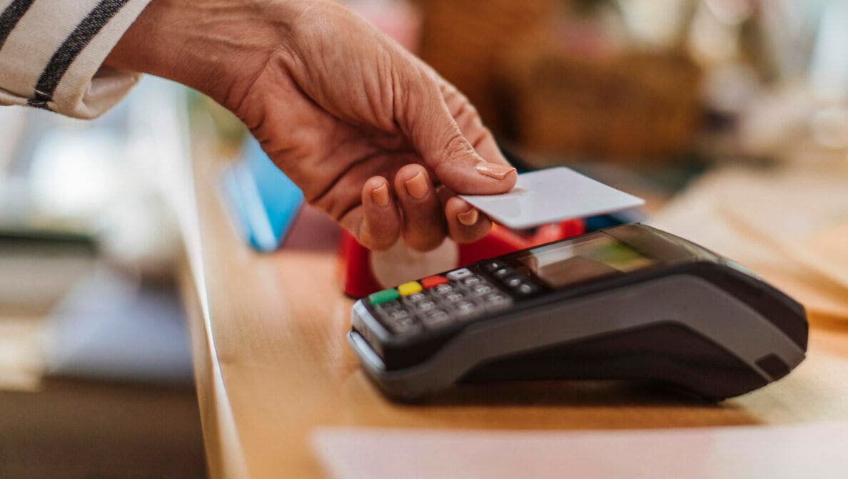 Eine Person hält eine Karte zum Bezahlen an ein Kartenlesegerät.