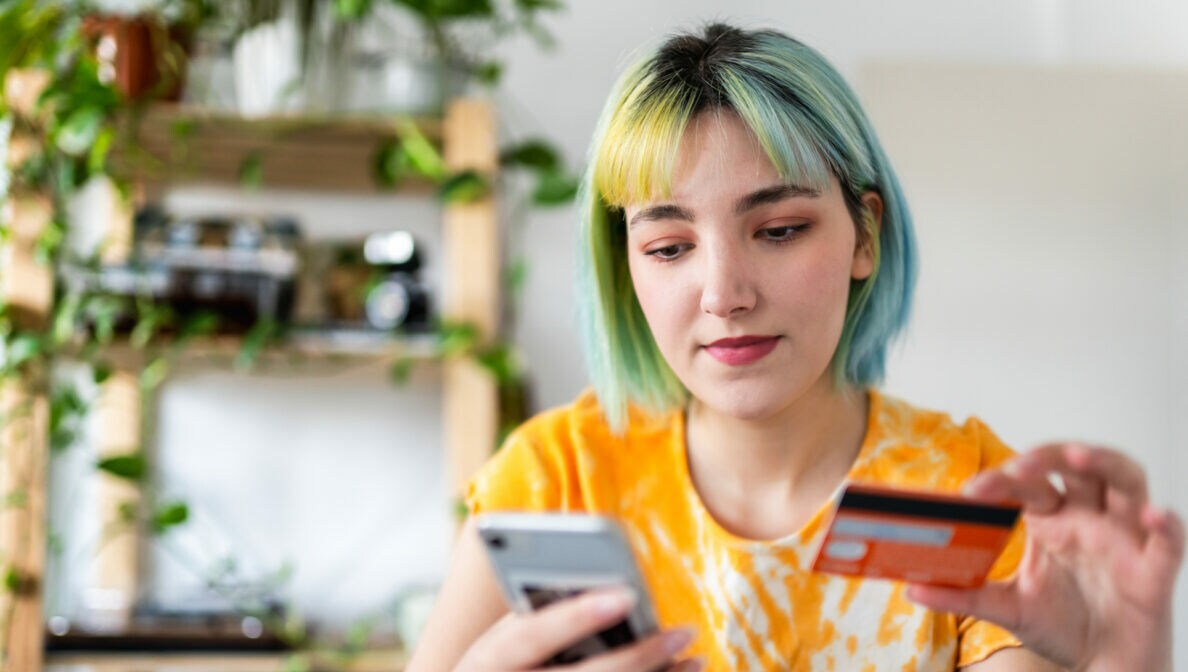 Nahaufnahme einer Person, die ein Smartphone sowie eine Bankkarte in den Händen hält.