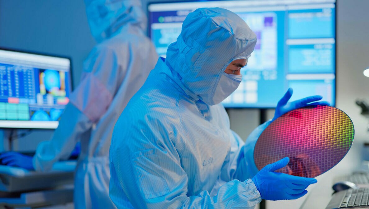 Eine Person im Laboranzug hält einen Wafer in seinen Händen.