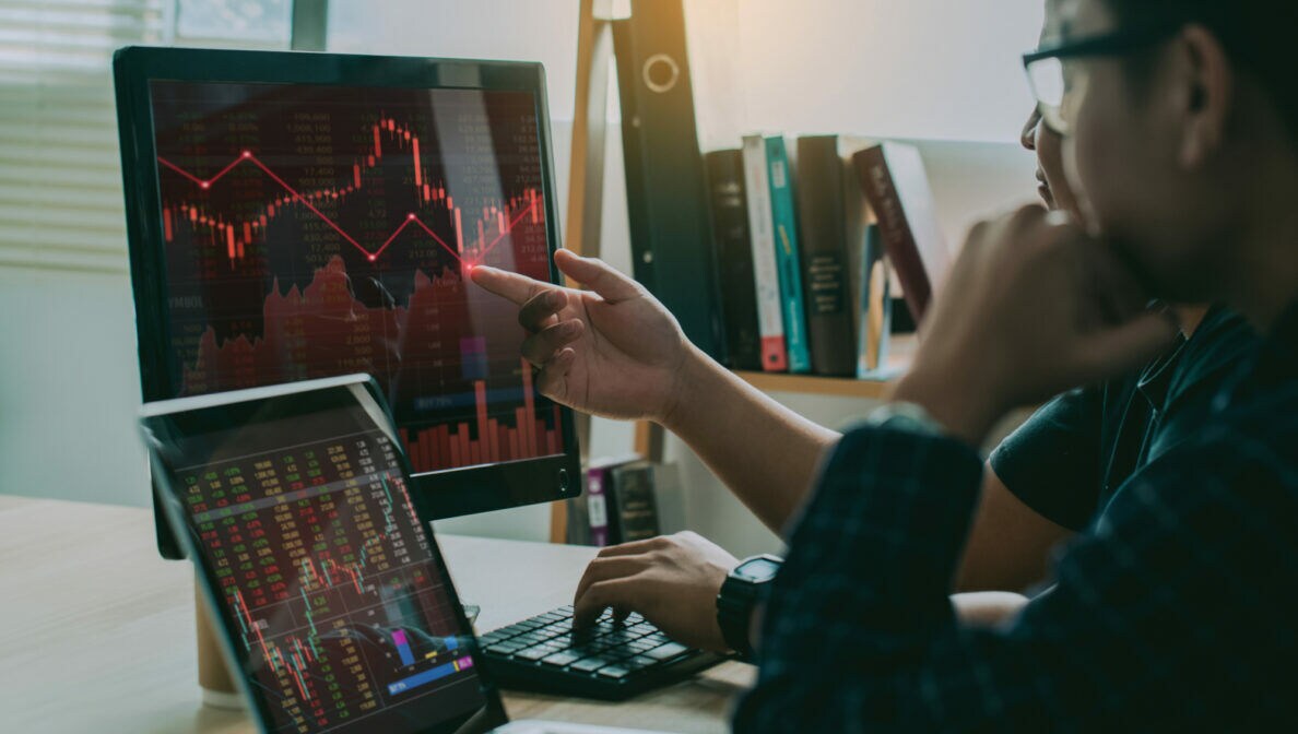 Zwei Personen sitzen vor Monitoren und schauen auf Aktienkurse.