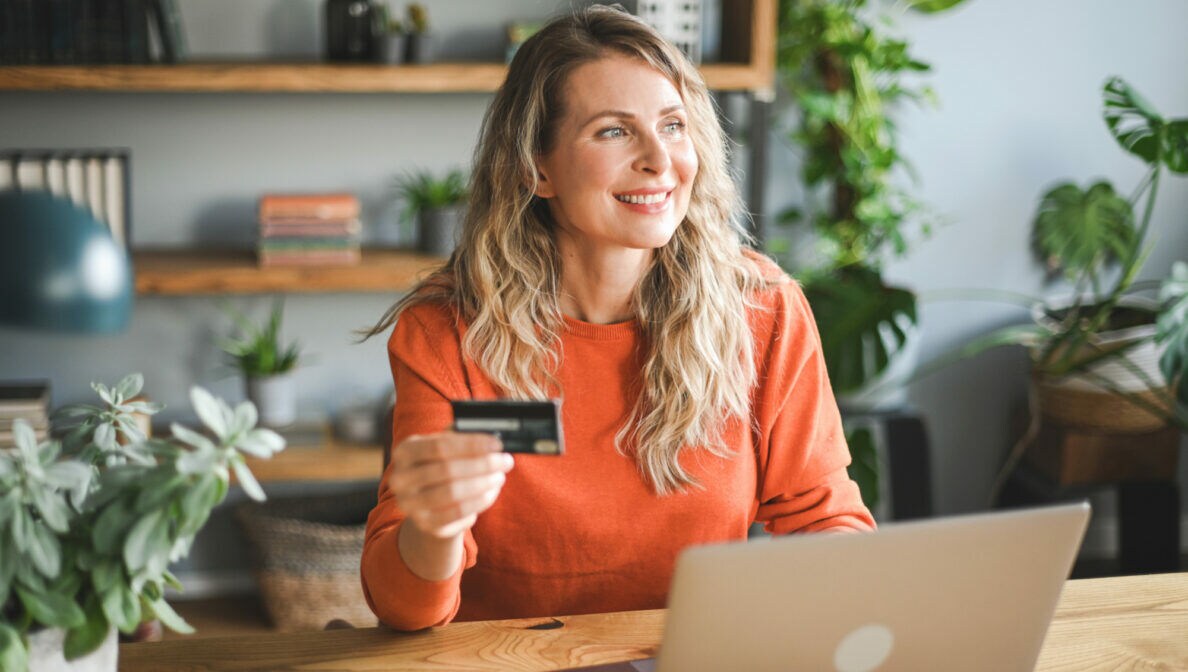 Eine Person sitzt vor einem geöffneten Laptop und hält eine Bankkarte in der Hand.