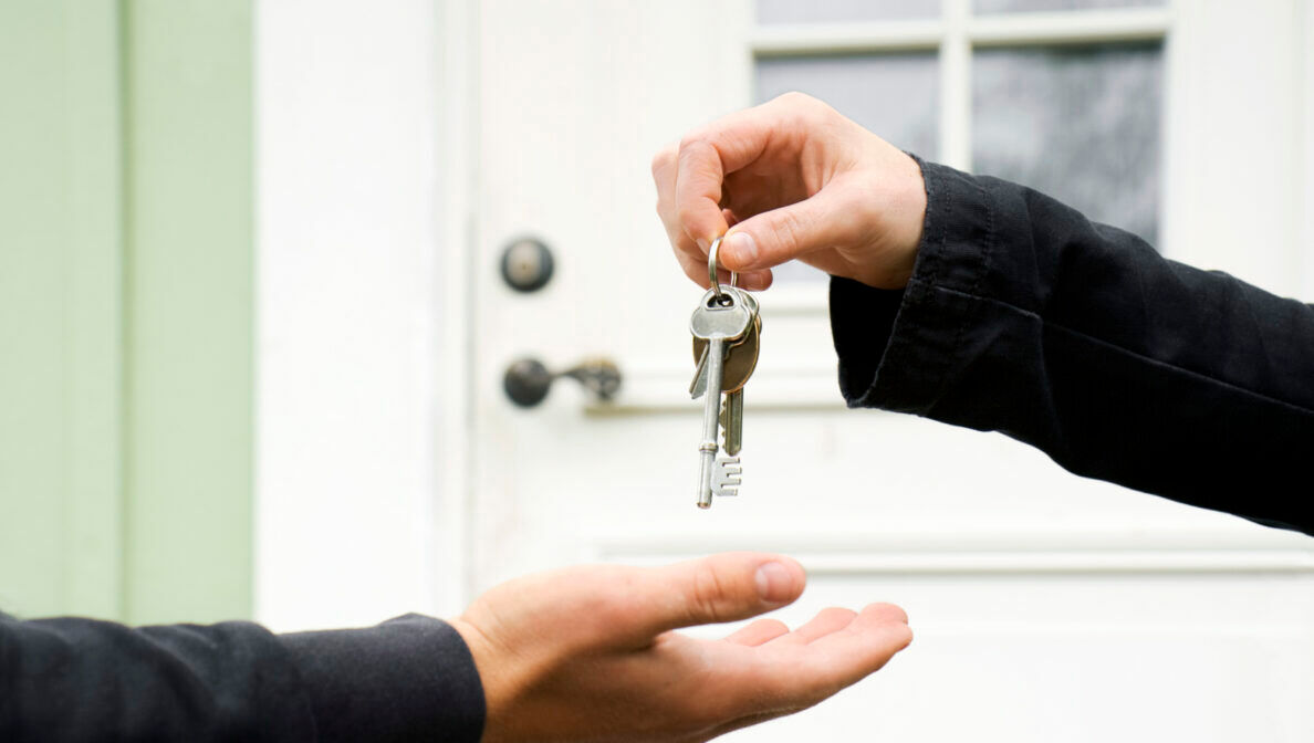 Eine Person übergibt vor einer Haustür einer anderen Person einen Schlüsselbund.