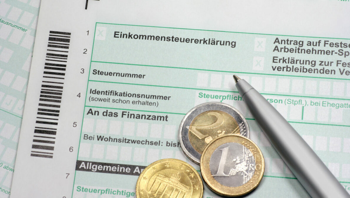 Drei Euromünzen liegen zusammen mit einem Kugelschreiber auf einem Dokument mit dem Titel Einskommenssteuererklärung.