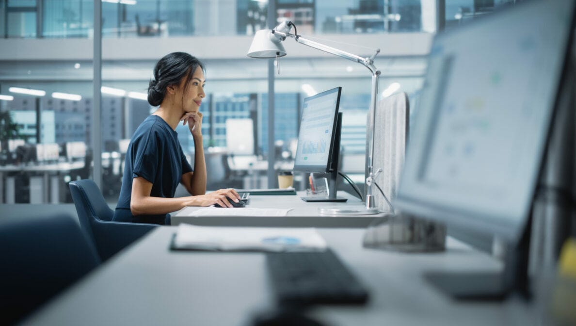 Eine junge Frau sitzt in einem Büro an einem Tisch mit Computer.