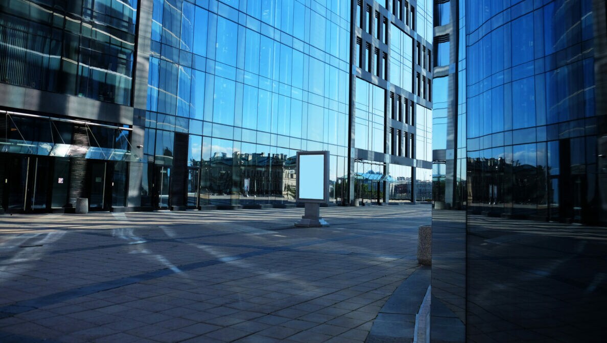 Mehrere verglaste Fassaden von modernen Bürogebäuden in der Sonne.