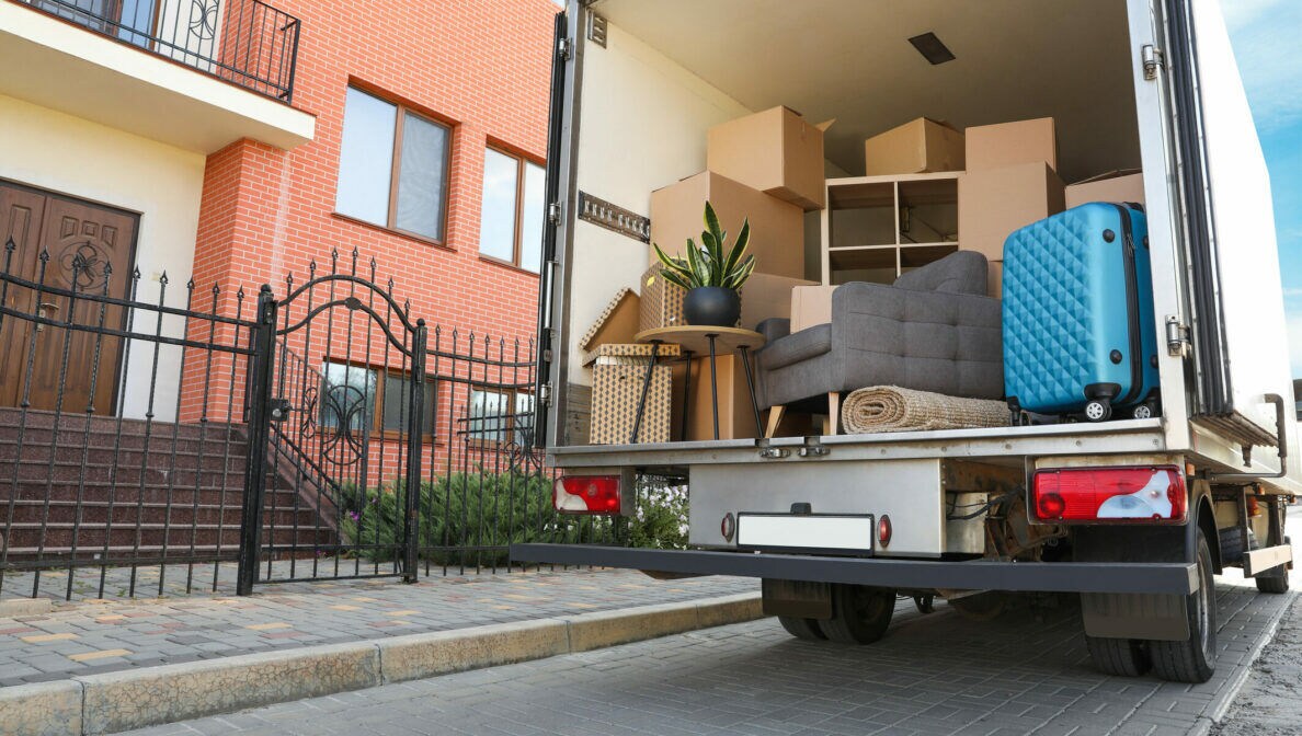Ein Umzugswagen steht vor einem Haus mit Backsteinfront. Im Wagen befinden sich einige Kartons, ein Regal, ein Sofa und weitere Einrichtungsgegenstände.