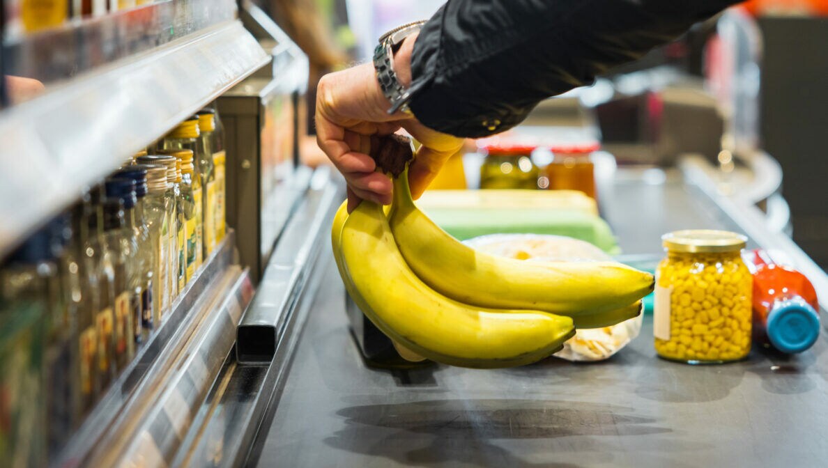 Eine Person steht an einer Supermarktkasse und legt Bananen auf das Förderband.