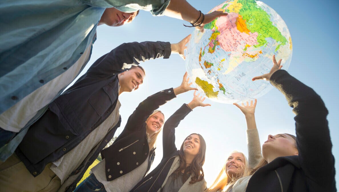 Eine Gruppe junger Leute halten gemeinsam ein Modell eines Globus in die Höhe.
